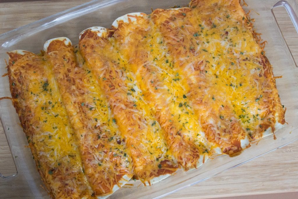 Six chicken enchiladas in glass casserole dish 