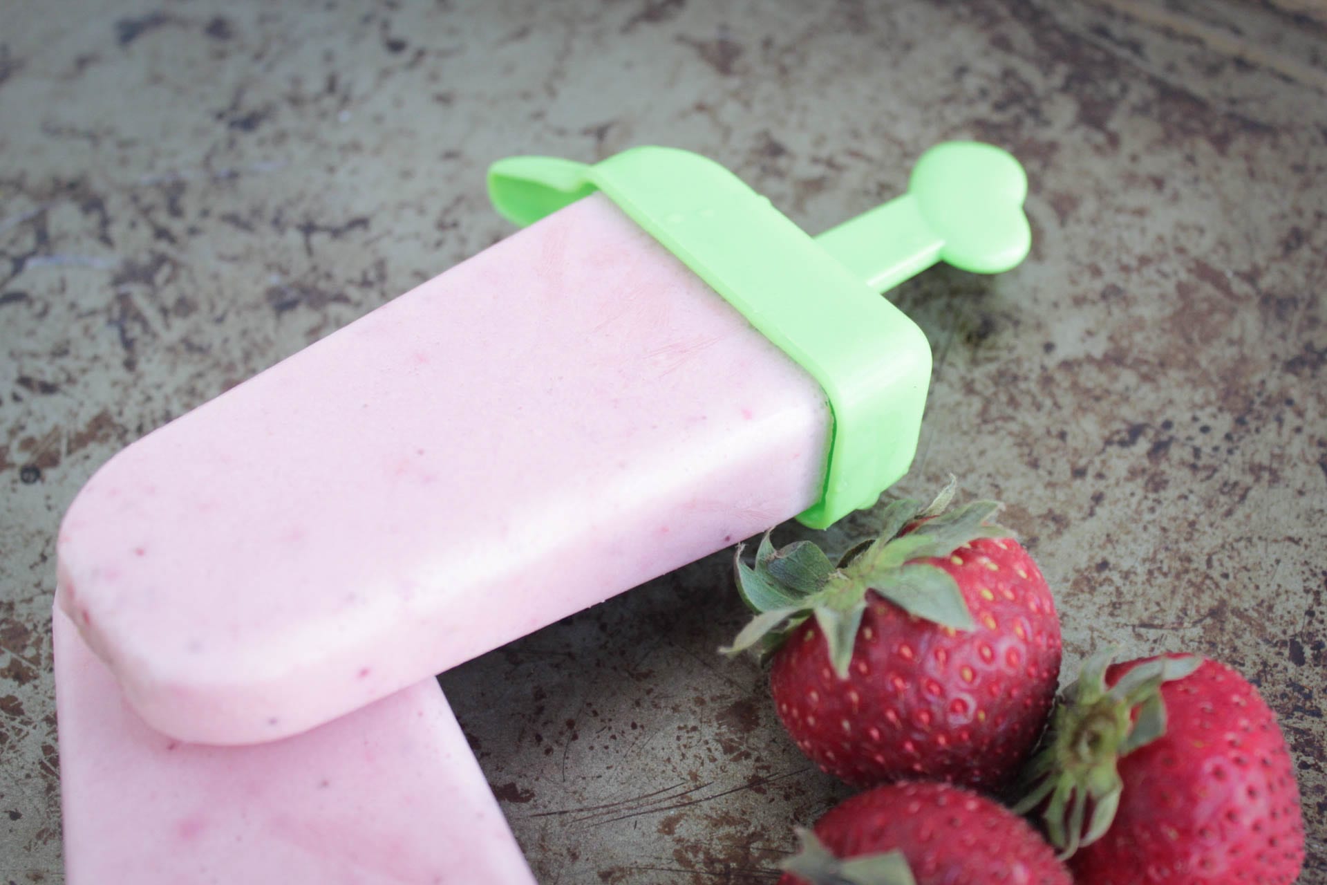 strawberry cheesecake popsicle in a popsicle mold with fresh strawberries
