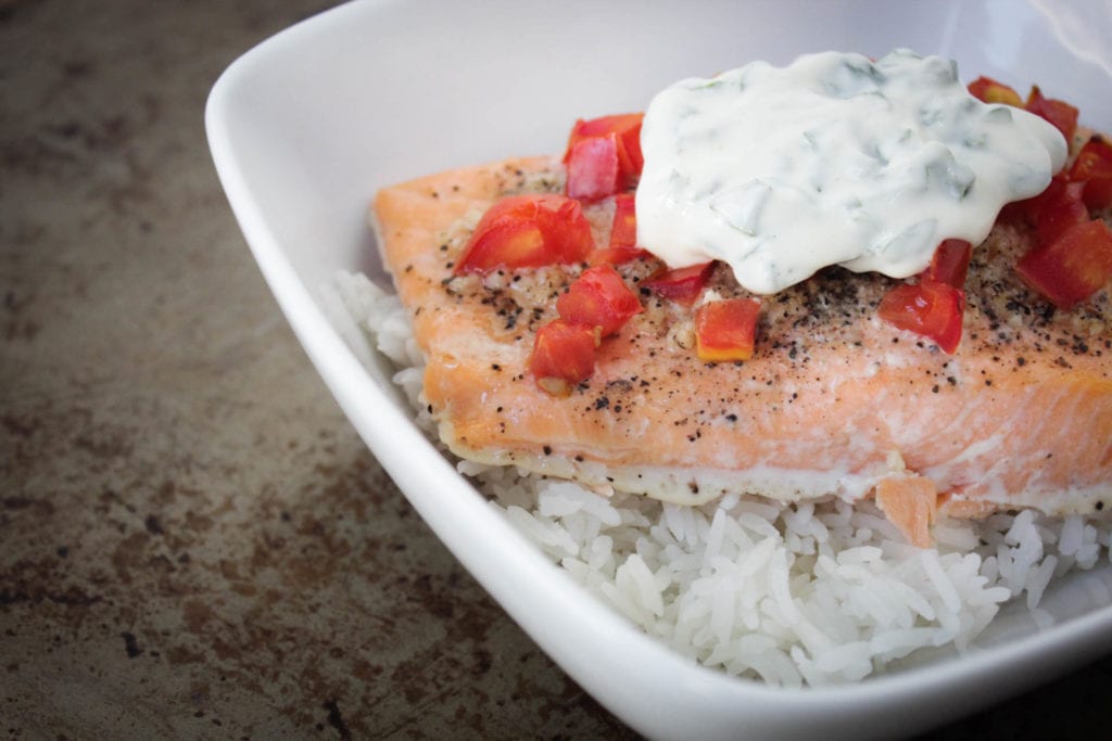 Baked salmon with tomatoes and basil mayo sauce over rice in a white bowl