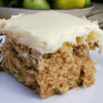 Slice of green tomato cake with cream cheese frosting on white plate