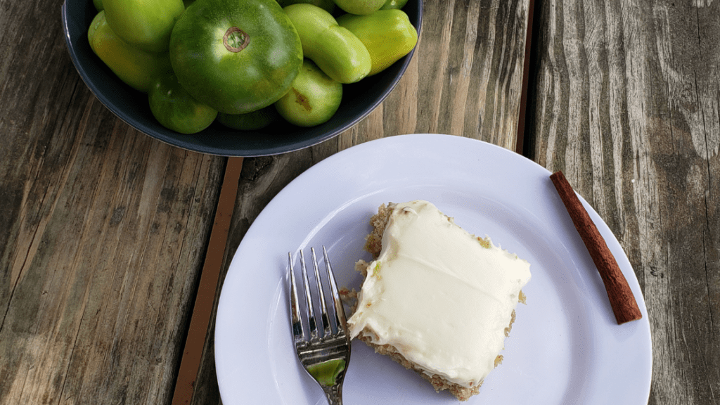 Plated green tomato cake with cream cheese frosting and bowl of green tomatoes