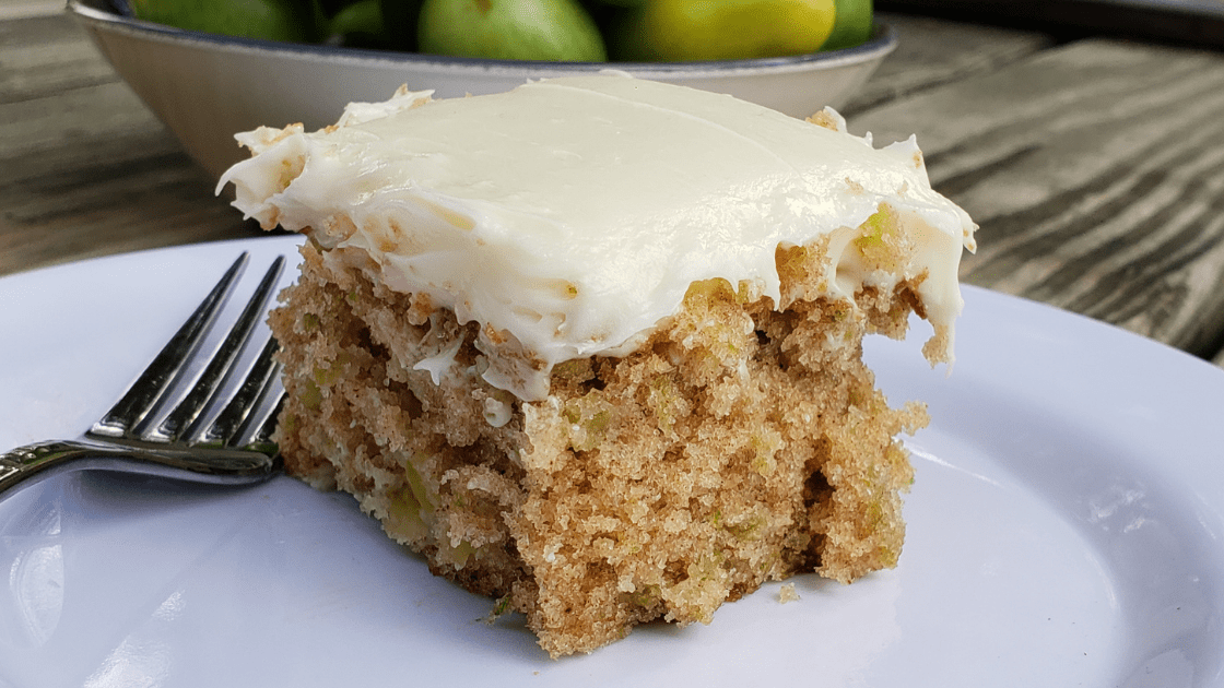 Slice of green tomato cake with cream cheese frosting on white plate