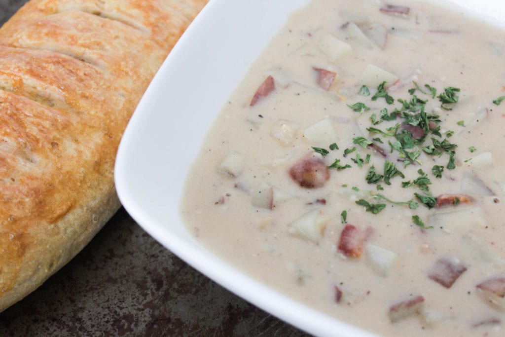 Creamy bacon potato soup in white bowl with French bread on the side