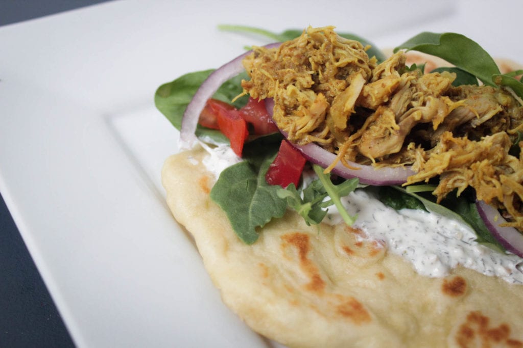 Crock pot chicken shawarma Indian cuisine served on naan or pita bread with greens, diced tomatoes, red onions and dill sauce