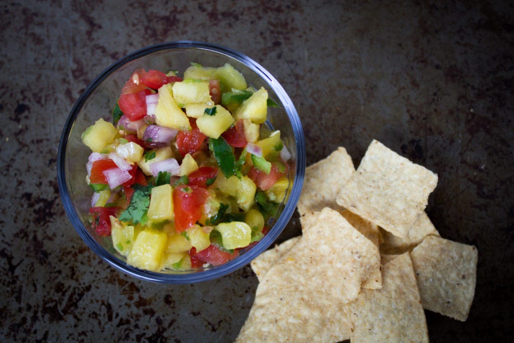 Bowl of pineapple salsa with fresh pineapple, tomatoes, red onion, jalapeno, cilantro and lime served with chips