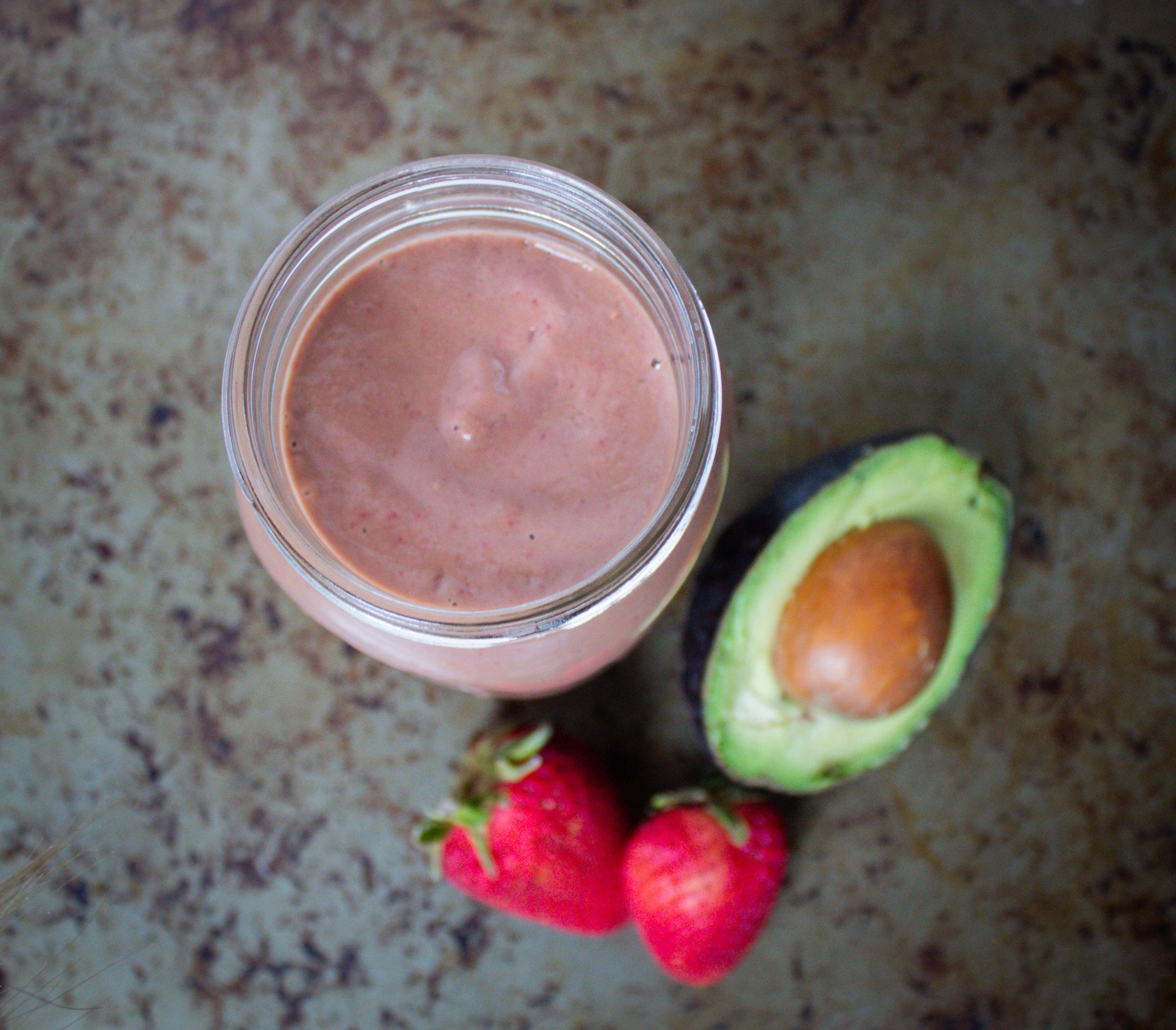 strawberry chocolate smoothie in glass jar with 2 fresh strawberries and 1/2 avocado next to it