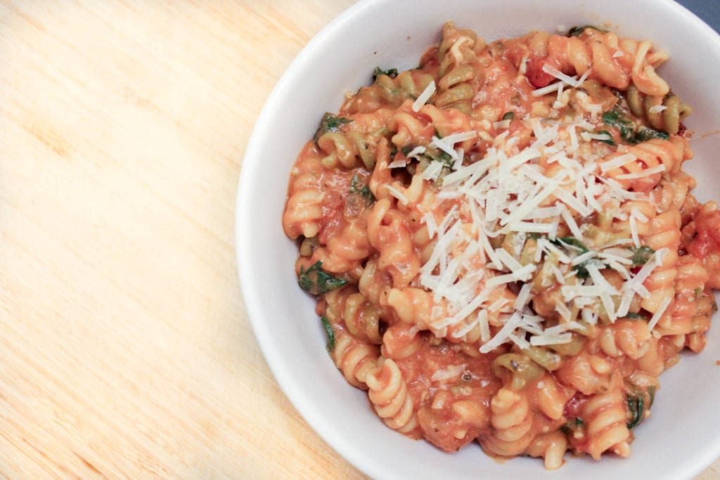 creamy tomata spinach pasta topped with parmesan cheese in white bowl