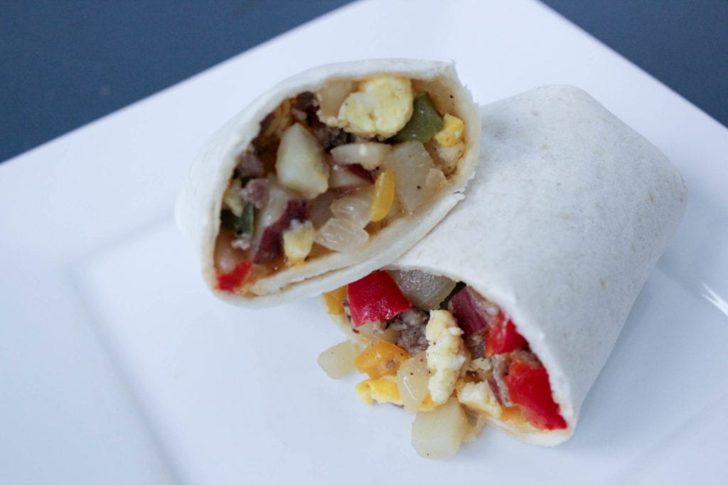 Sausage, eggs, potatoes, onion and red bell pepper in a tortilla on a white plate