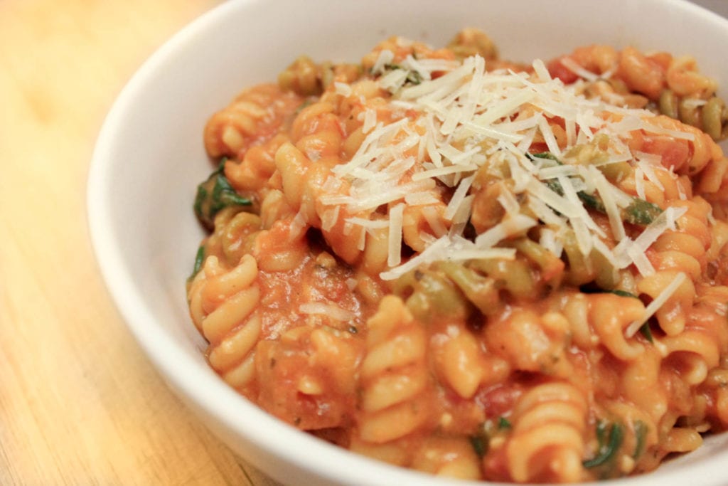 Creamy pasta dish with spinach and tomatoes topped with Parmesan cheese and served in white bowl