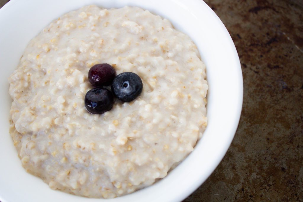 steel cut oats in white bowl with 3 blueberries on top