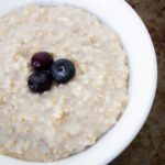 steel cut oats in white bowl with 3 blueberries on top