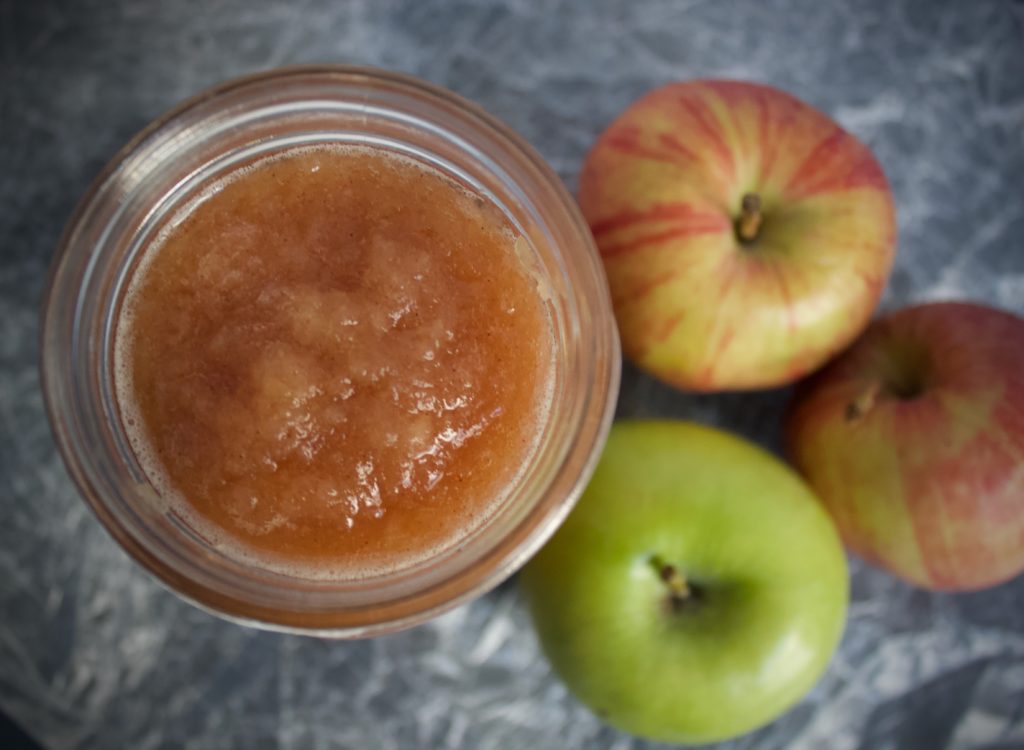 homemade pressure cooked applesauce in a jar on a table next to 3 apples