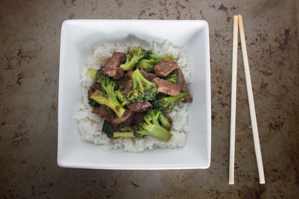 Steak tips and broccoli served over rice in a square bowl with chopsticks placed next to the bowl