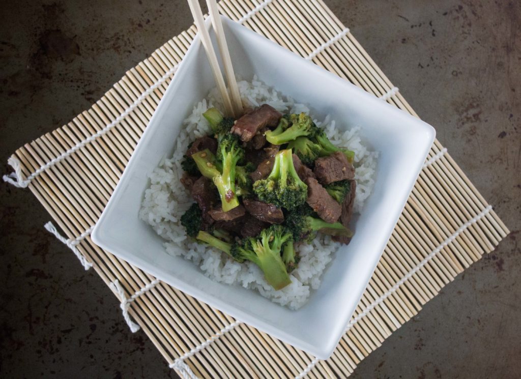 Beef and broccoli over white rice in square bowl with chopsticks