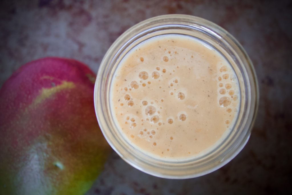 Citrus mango smoothie in glass cup next to mango