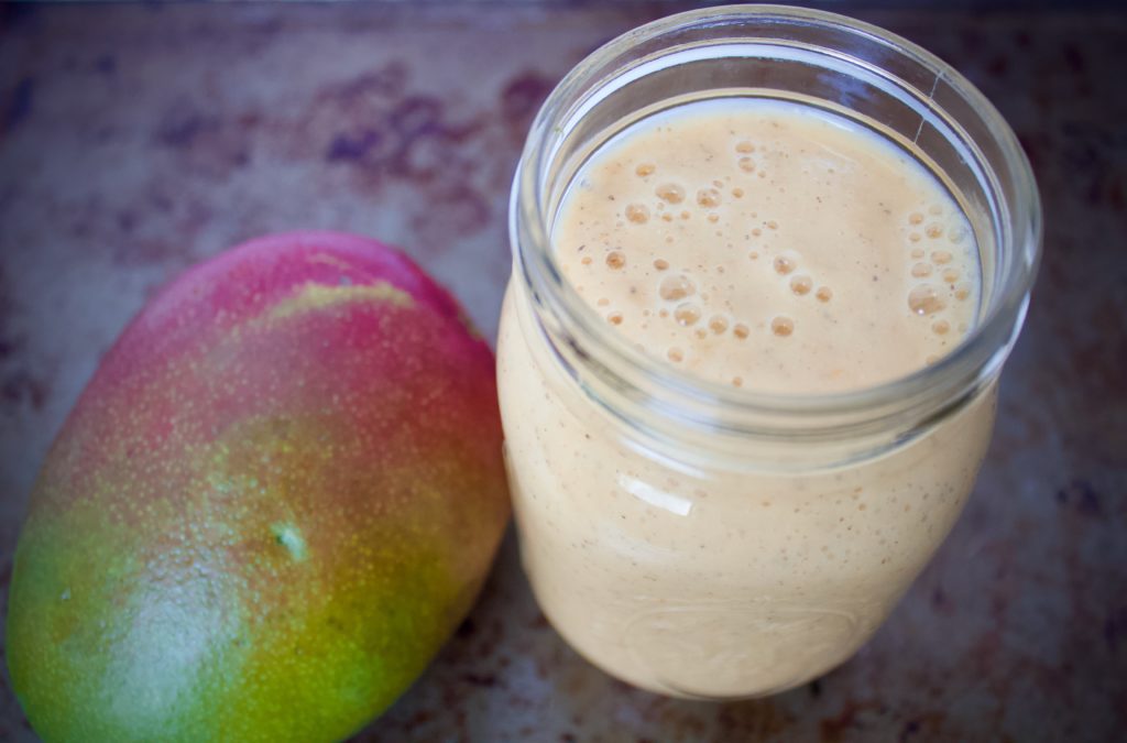 citrus mango smoothie in glass jar next to mango