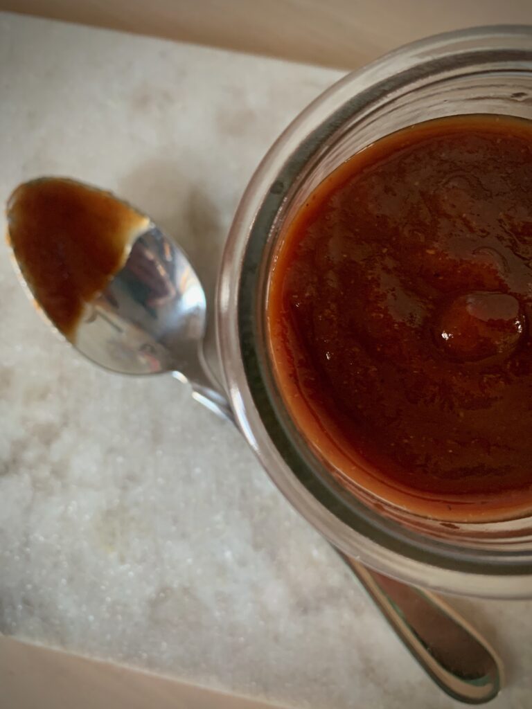 Homemade BBQ sauce in glass jar next to silver spoon
