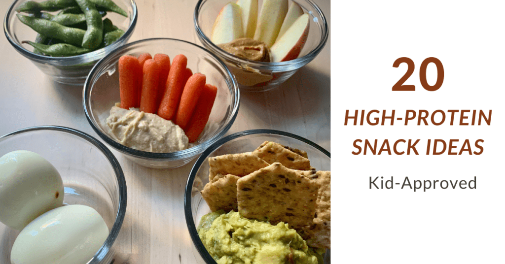 5 clear glass bowls with high-protein snacks including steamed edamame, apples with peanut butter, whole wheat crackers with guacamole, carrots with hummus and hard boiled eggs