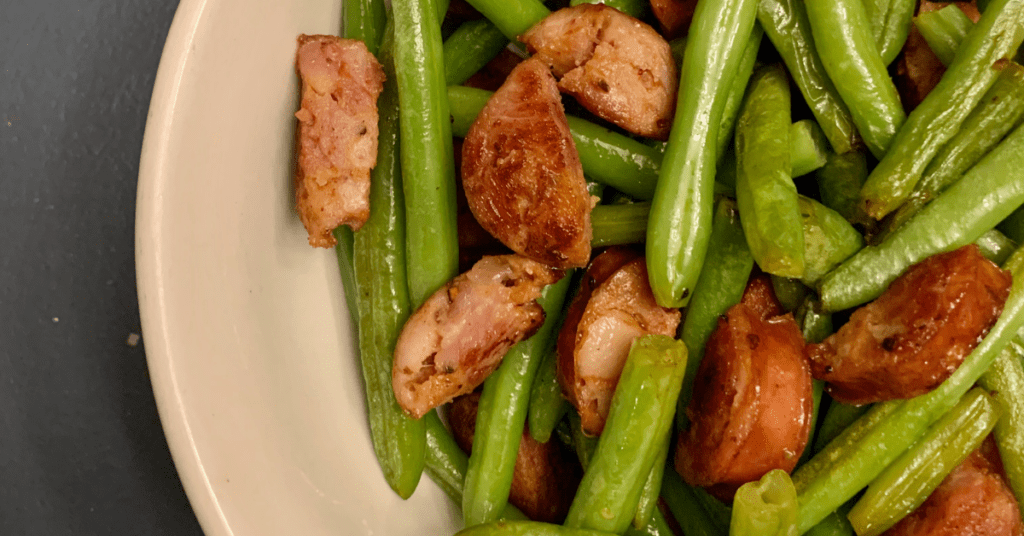 cooked green beans and sausage in a white bowl