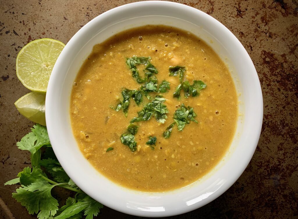 White bowl with lentil curry soup next to lime wedges and cilantro.