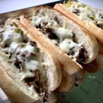 3 philly cheesesteaks on a baking sheet with melted cheese