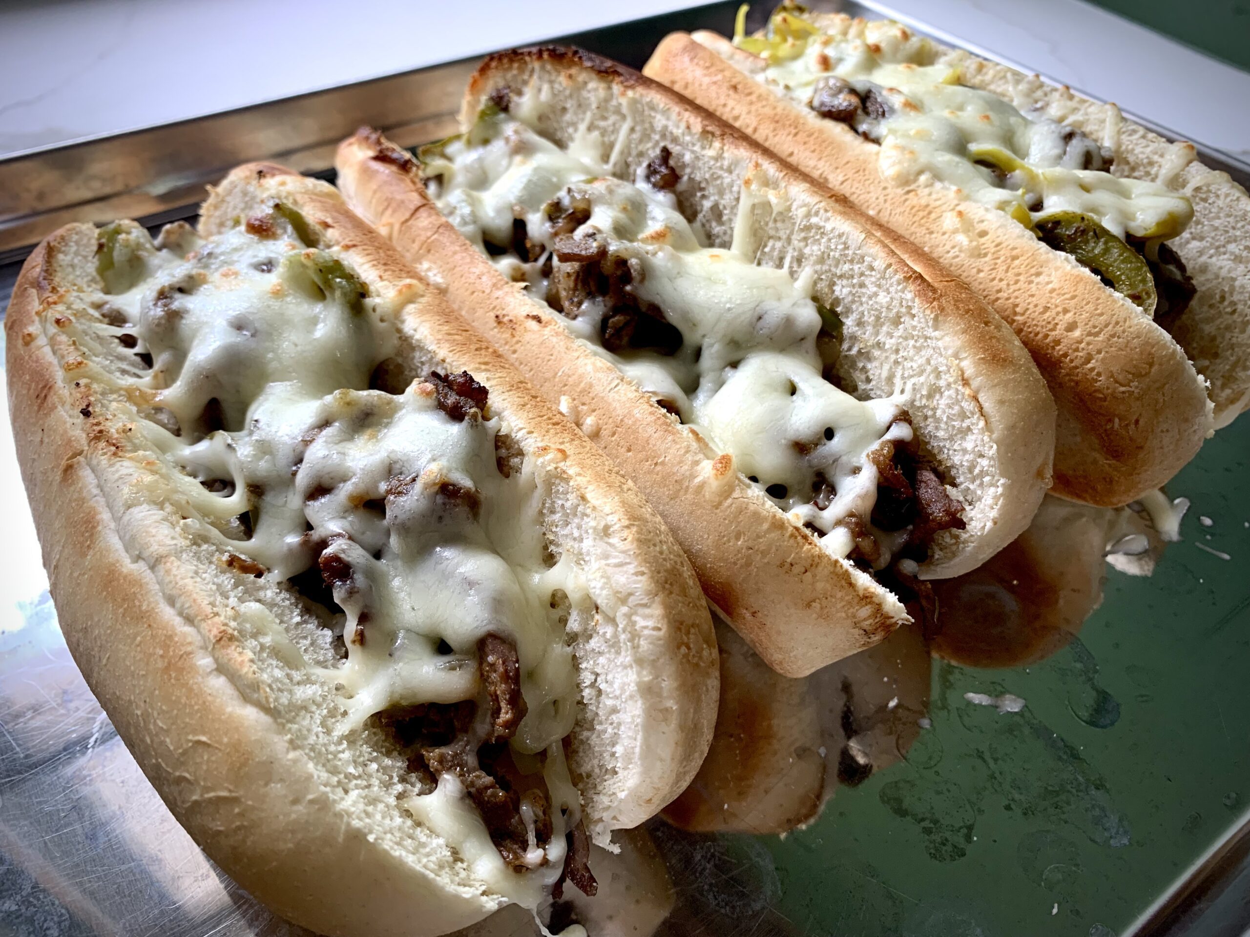 3 philly cheesesteaks on a baking sheet with melted cheese